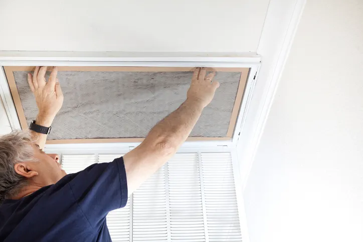 HVAC technician performing AC repair in Gladstone, MO by replacing a dirty air filter in a ceiling vent to improve air quality and system efficiency.